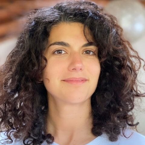 Portrait of a person with curly dark hair, slight smile, and a light background