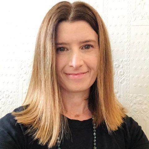 Portrait of a smiling woman with straight shoulder-length hair against a light textured wall