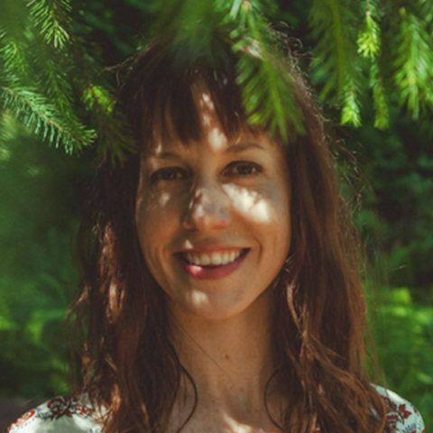 Smiling woman with brown hair framed by green tree branches outdoors