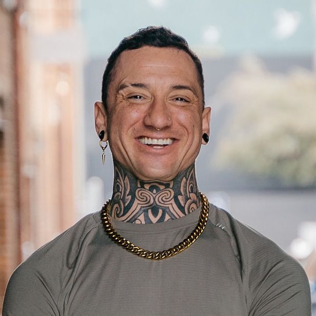 Smiling person with neck tattoos, gold chain, and gray shirt in a bright indoor setting