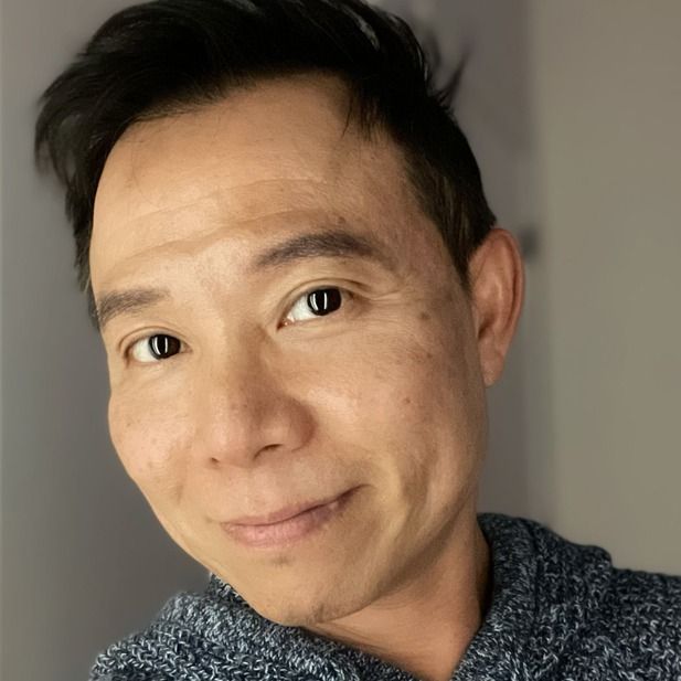 Close-up portrait of a smiling person in a blue textured sweater against a gray background