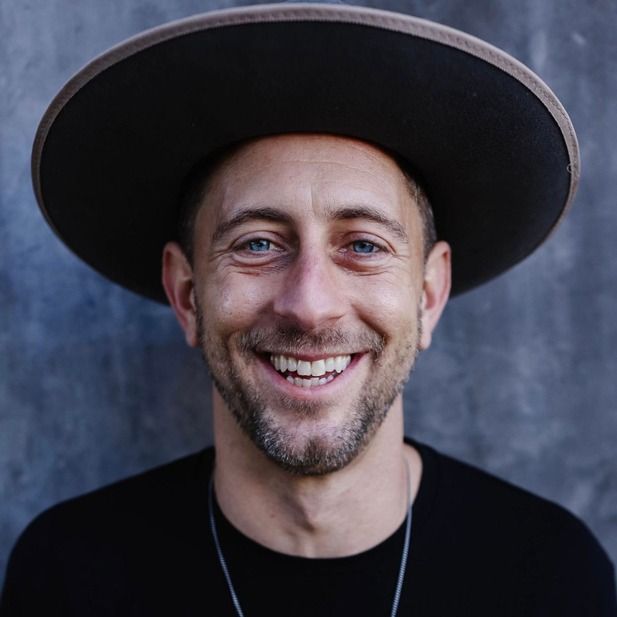 Smiling man in a wide-brim hat against a textured gray background