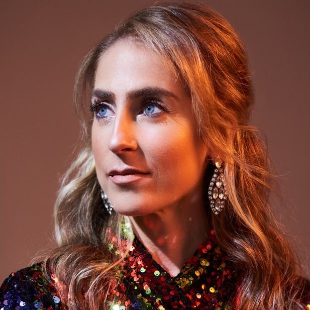 Portrait of a woman in a sequined top and dangling earrings, looking off to the side against a warm background