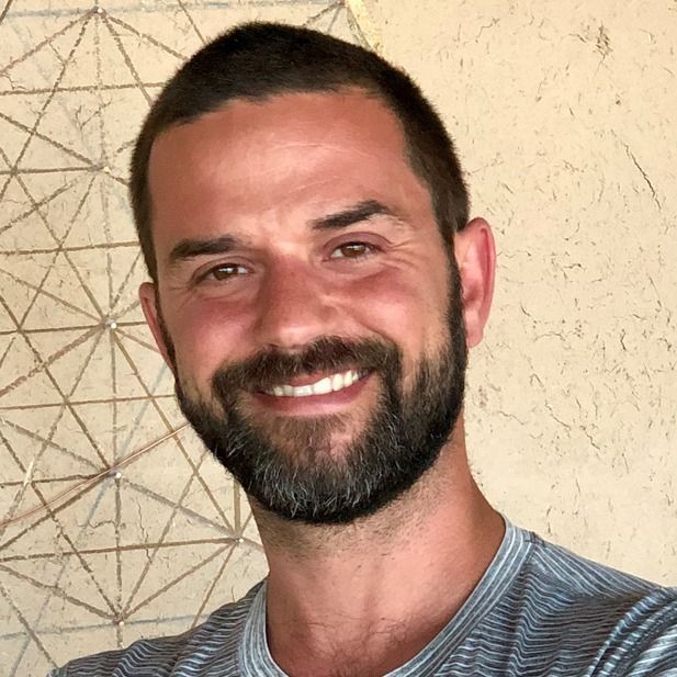 Smiling bearded man in a striped shirt against a beige wall with geometric line art