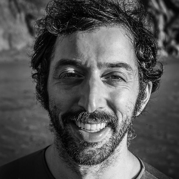 Black-and-white close-up portrait of a smiling man outdoors with a blurred background