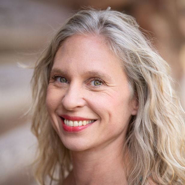 Smiling woman with wavy blonde hair against a softly blurred outdoor background
