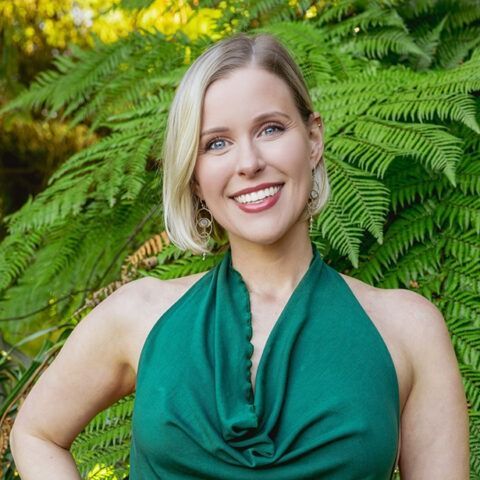 Smiling woman in a green halter top standing before lush fern foliage.
