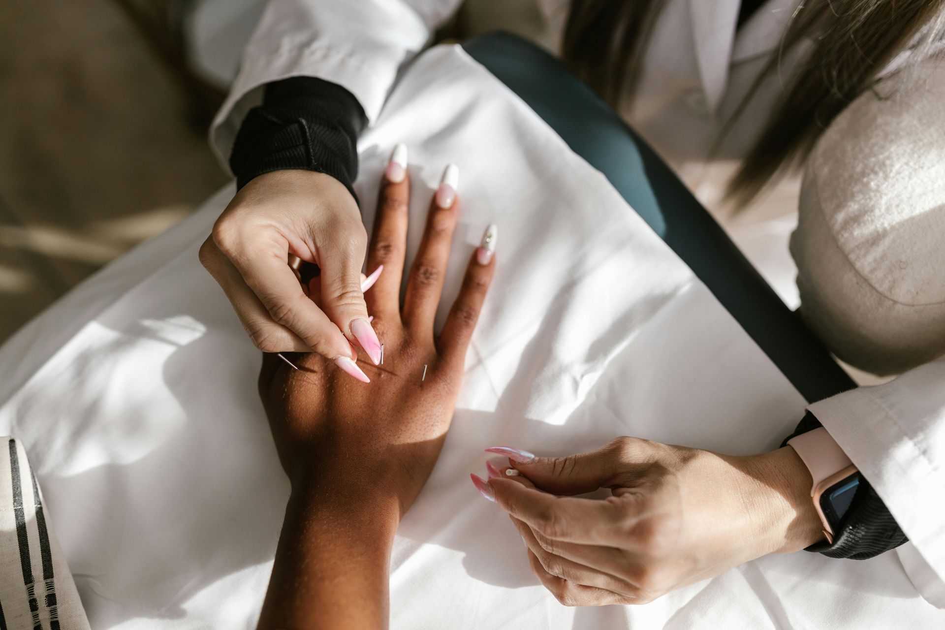 Hands painting fingernails on a dark-skinned hand resting on a white towel