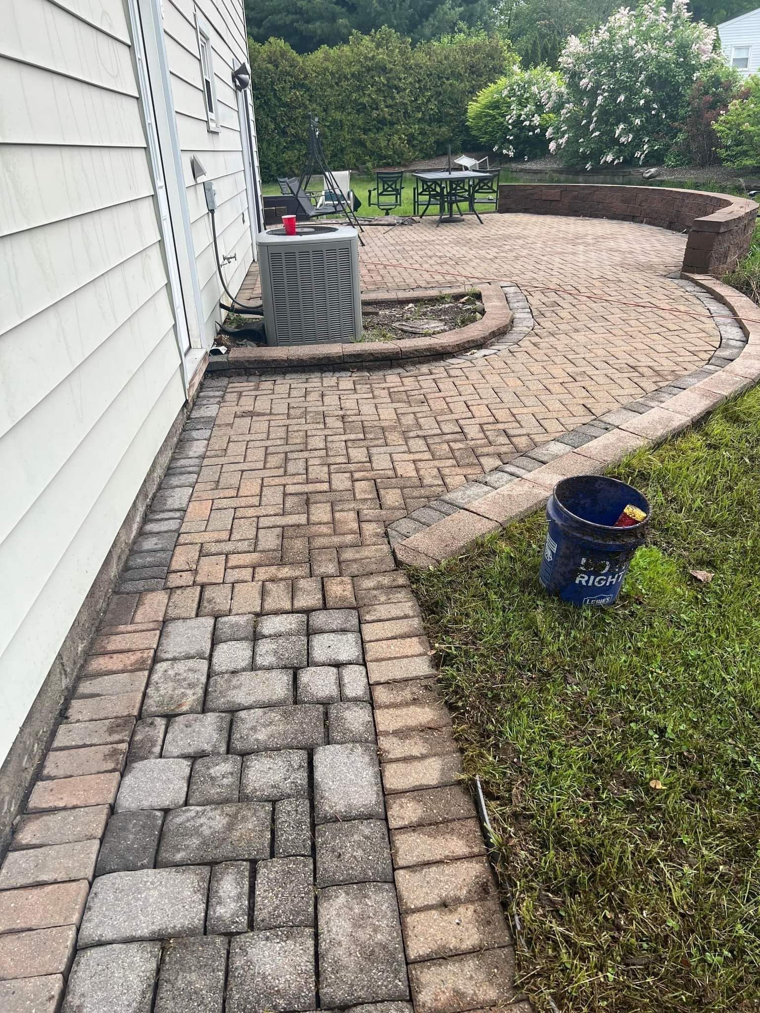 Brick pathway and patio next to a white house and green grass, with an AC unit.