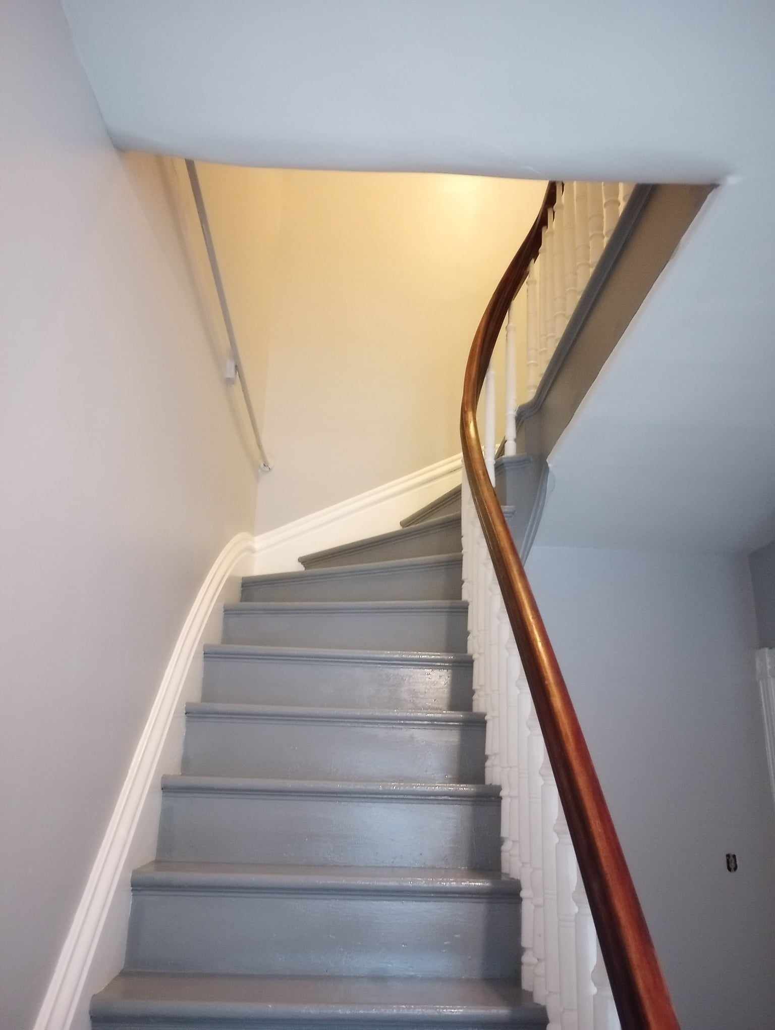 Grey staircase with wooden handrail curves up to a ceiling opening.