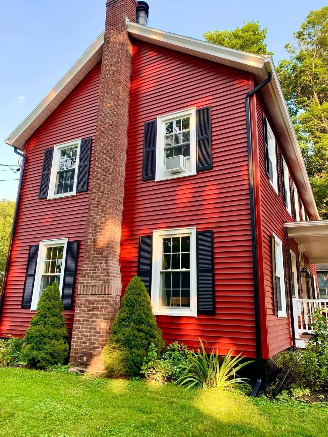 Red two-story house with black shutters, white trim, and a brick chimney. Green lawn in front.
