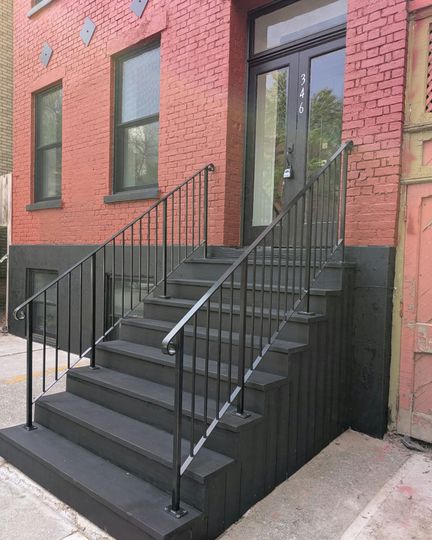 Exterior of a red brick building with black painted stairs and railing leading to a double door entrance.