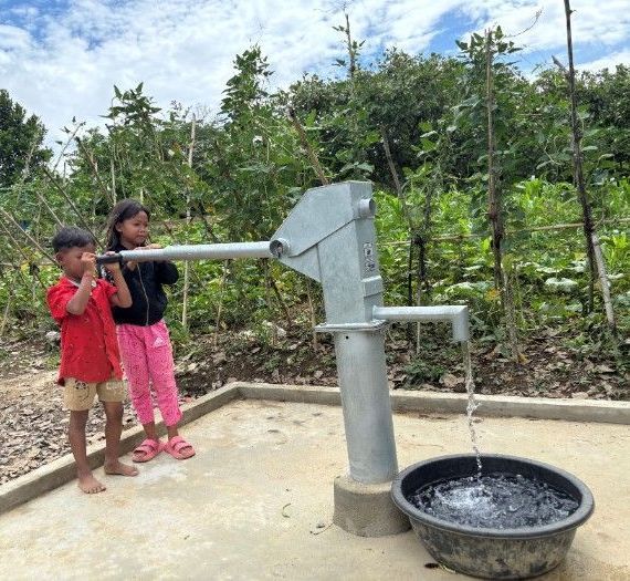 A boy and a girl are standing next to a water pump.