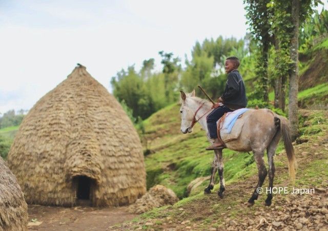 A man is riding a horse in front of a hut.