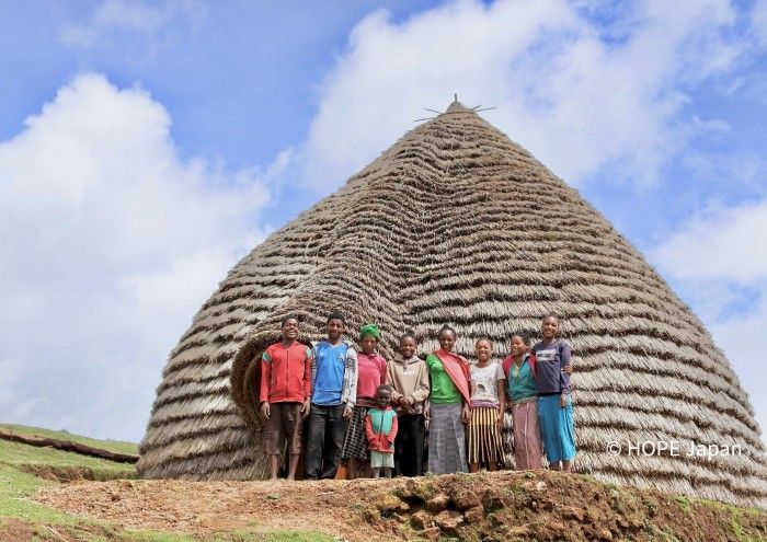 A group of people are standing in front of an Ethiopian home.