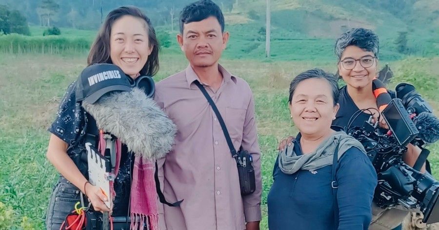 Four people smiling for a photo in a field, one holding a boom mic.