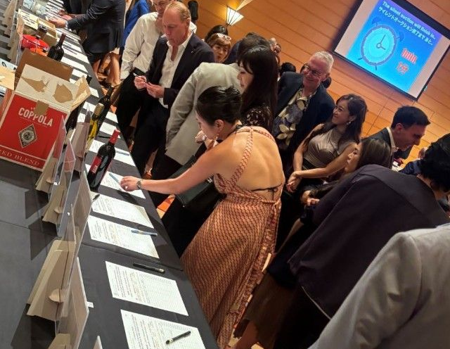 People at a wine auction, placing bids on a long table.