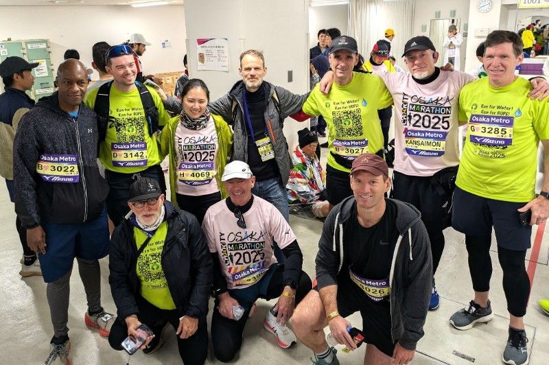 A group of HOPE Runners are posing for a picture in a room at the 2025 Osaka Marathon.
