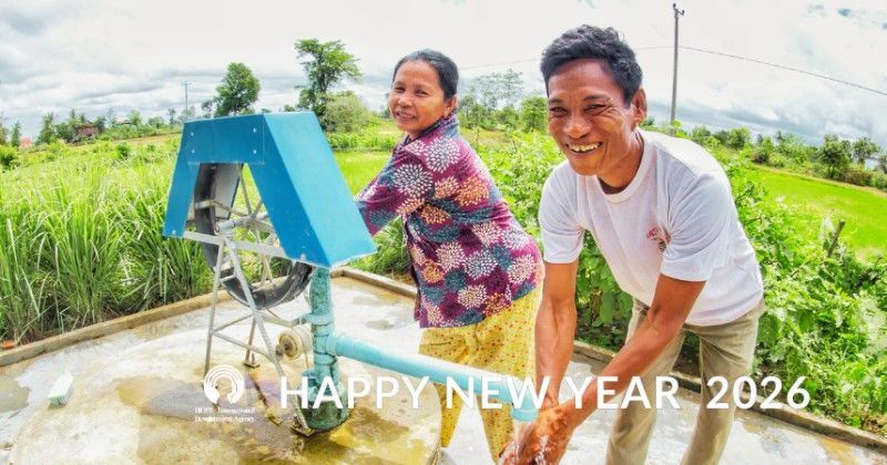 A man and woman smiling next to a blue water pump outdoors; 