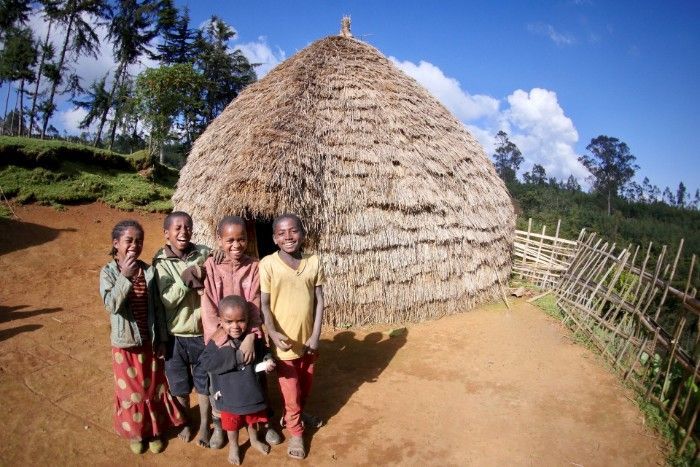 A group of children are posing for a picture in front of a thatched hut.