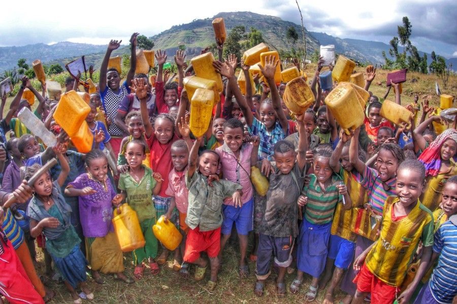 A large group of Ethiopia children are standing in a field holding buckets in their hands.