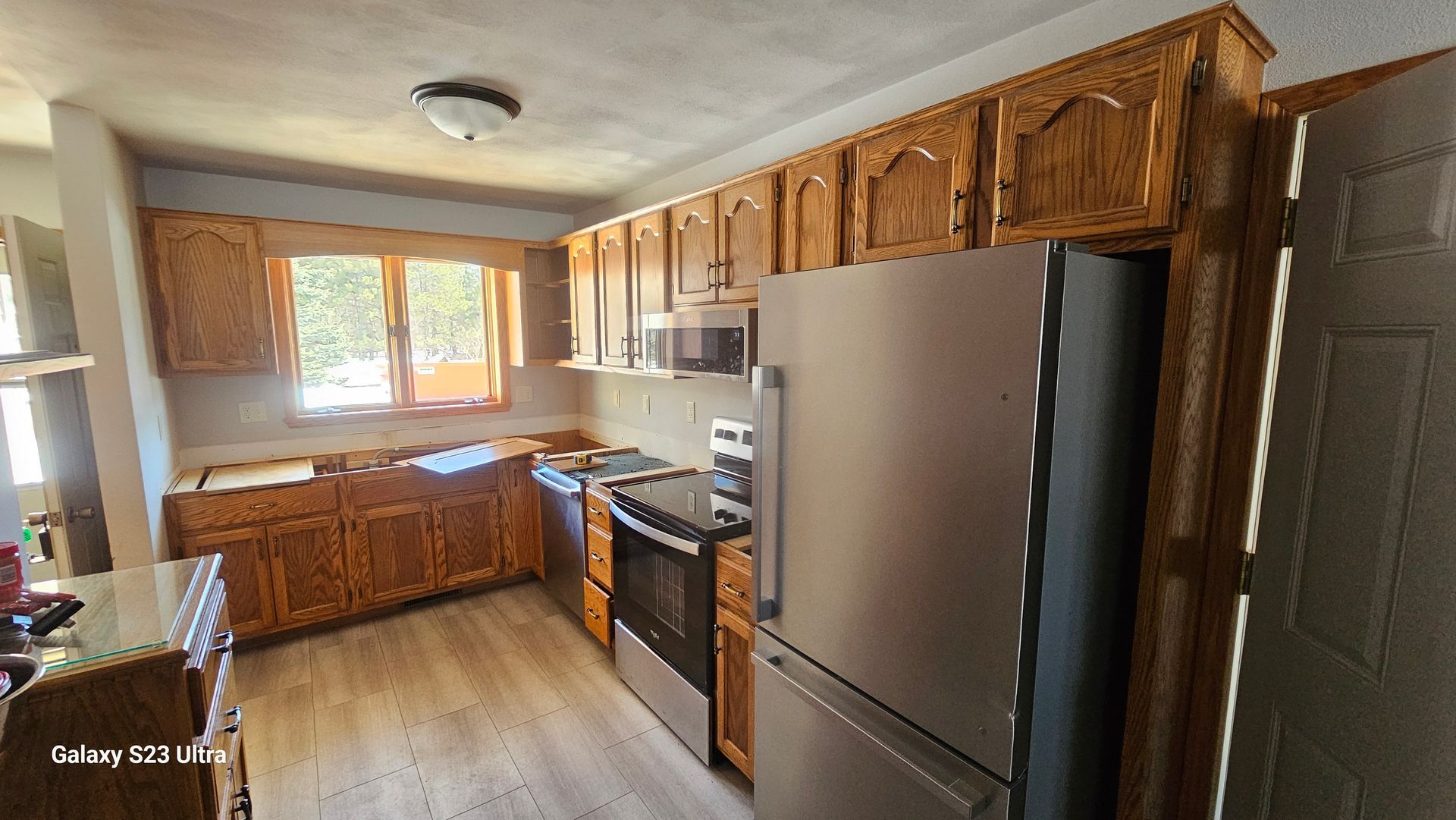 A kitchen with light wood cabinets, stainless steel appliances, and a window above the counter.