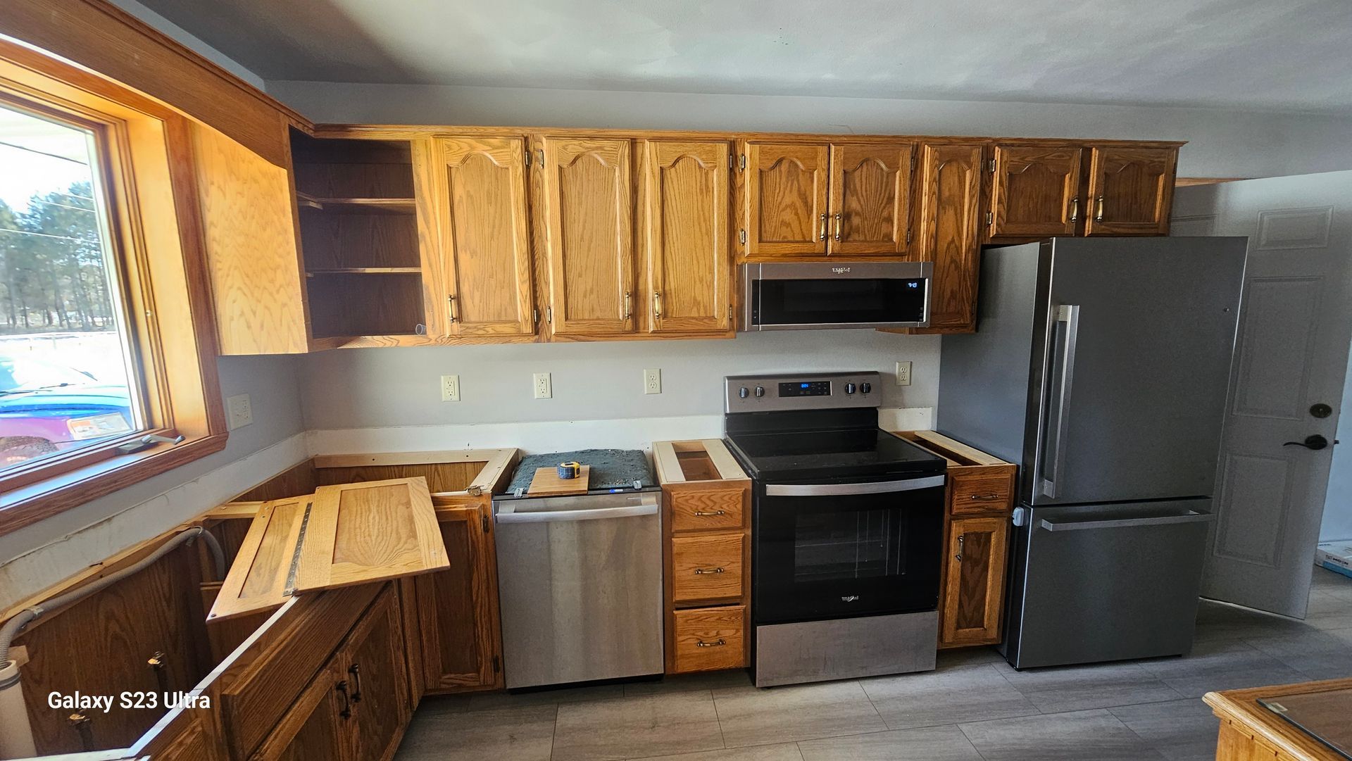 A kitchen featuring oak cabinets, stainless steel appliances, a gray refrigerator, and light gray vinyl flooring.