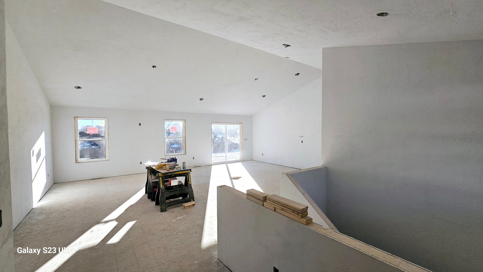 An unfinished interior room with freshly painted white walls, recessed lighting, and construction tools on a workbench.