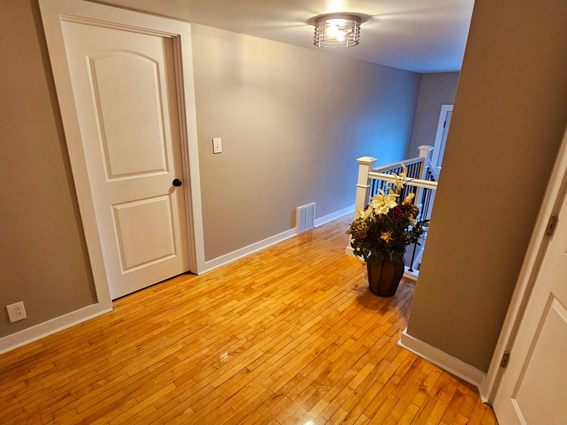 A hallway with hardwood floors and a vase of flowers on the floor