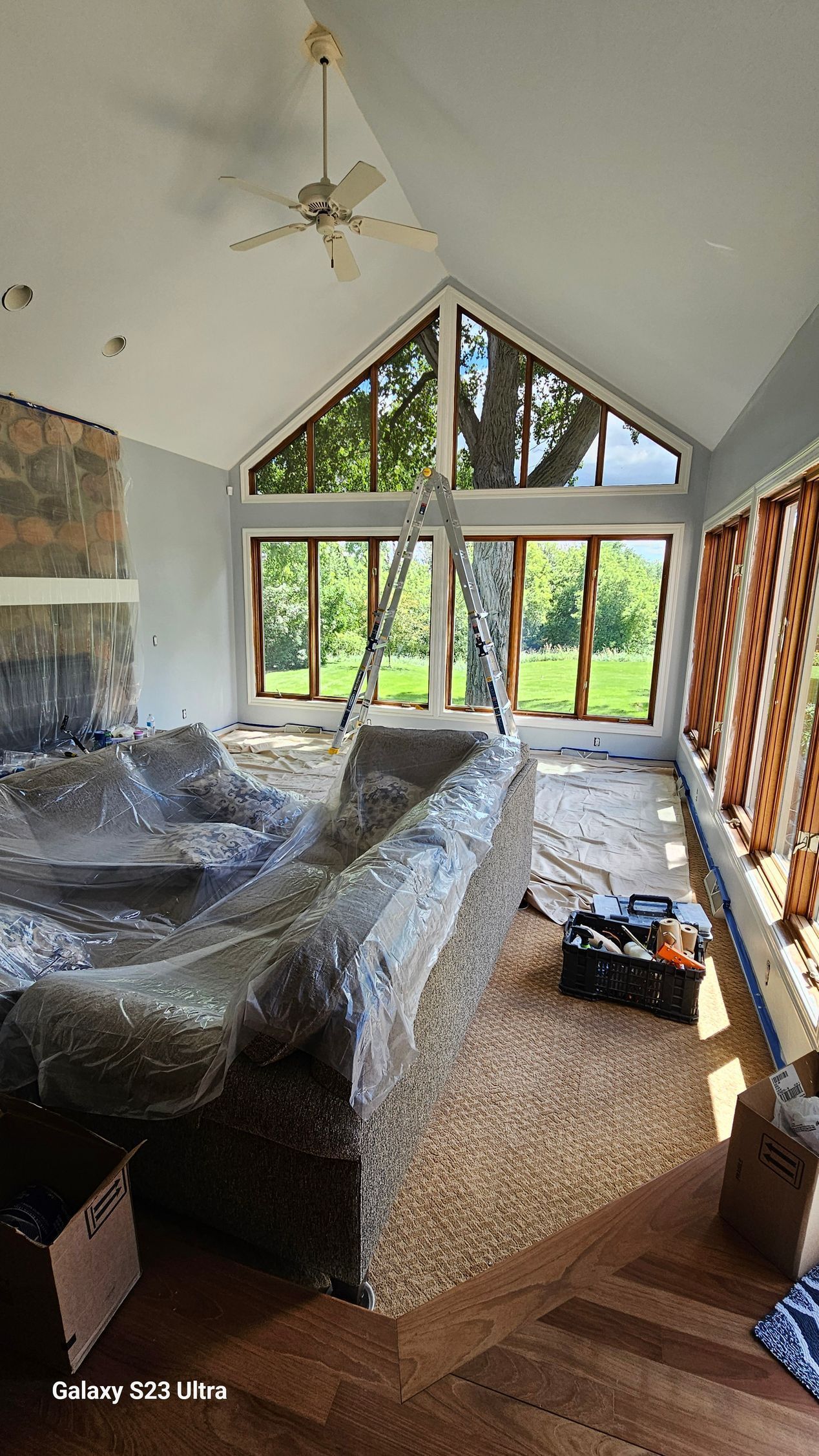 A living room with a couch wrapped in plastic and a ladder
