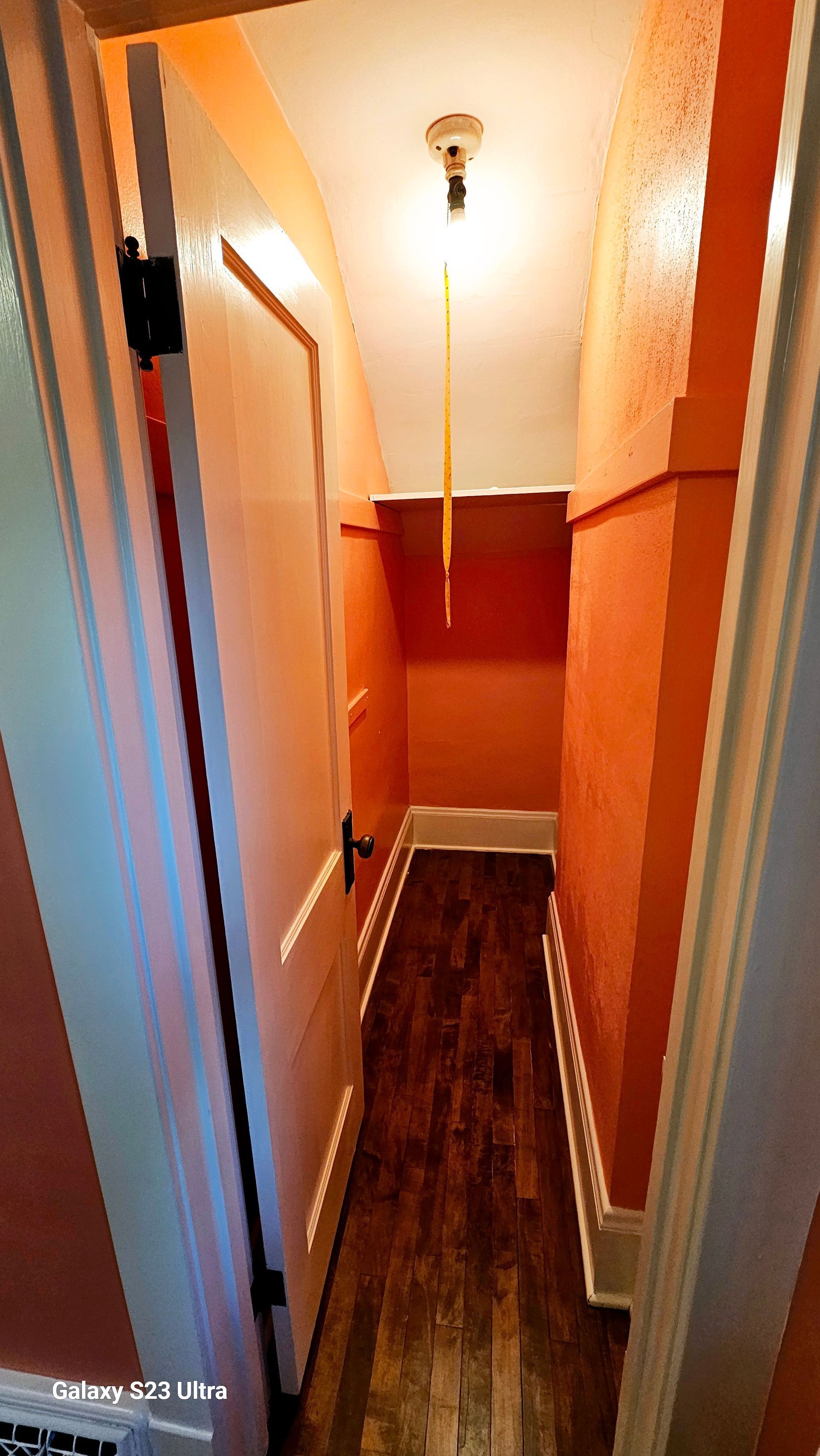 A narrow hallway with orange walls and wooden floors in a house