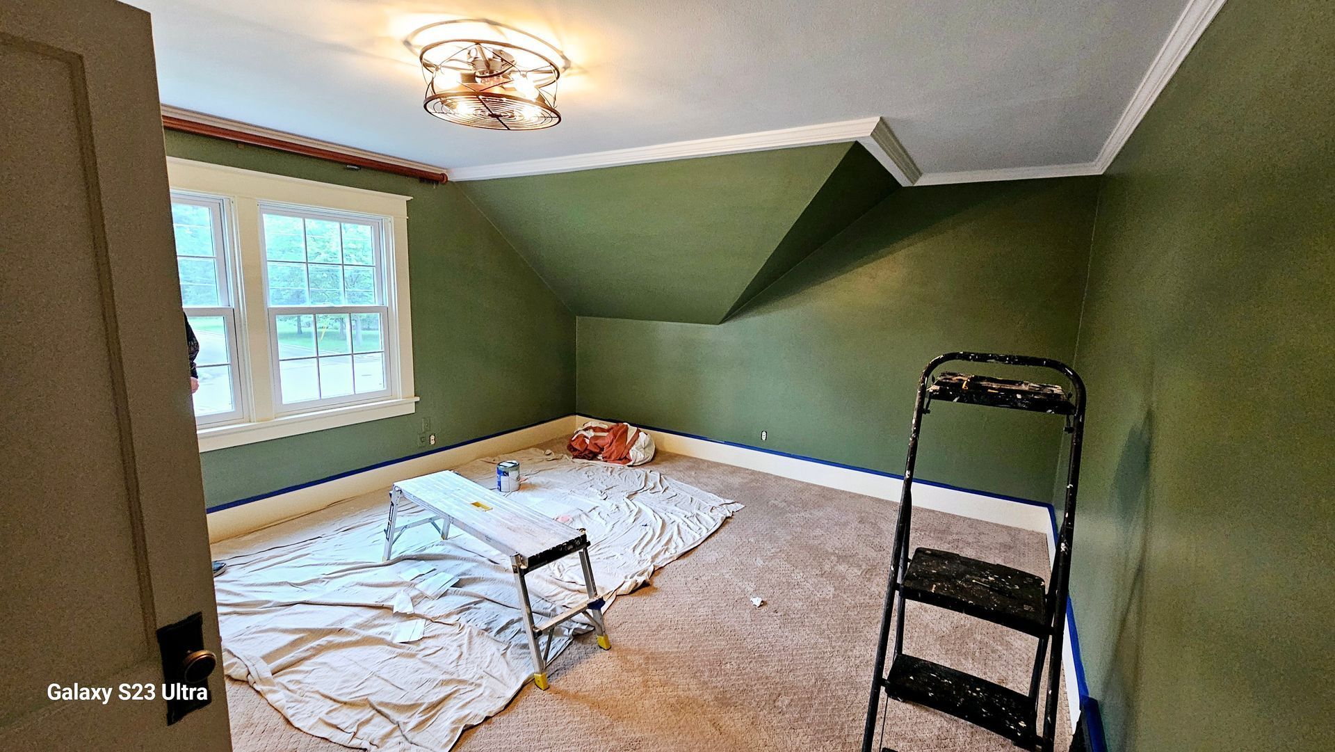 A room with green walls and a ladder in it is being painted