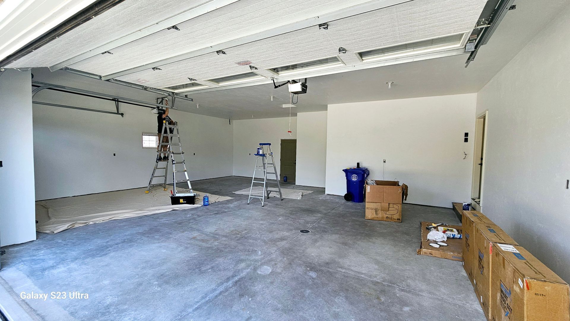 An empty garage with a ladder and a blue trash can