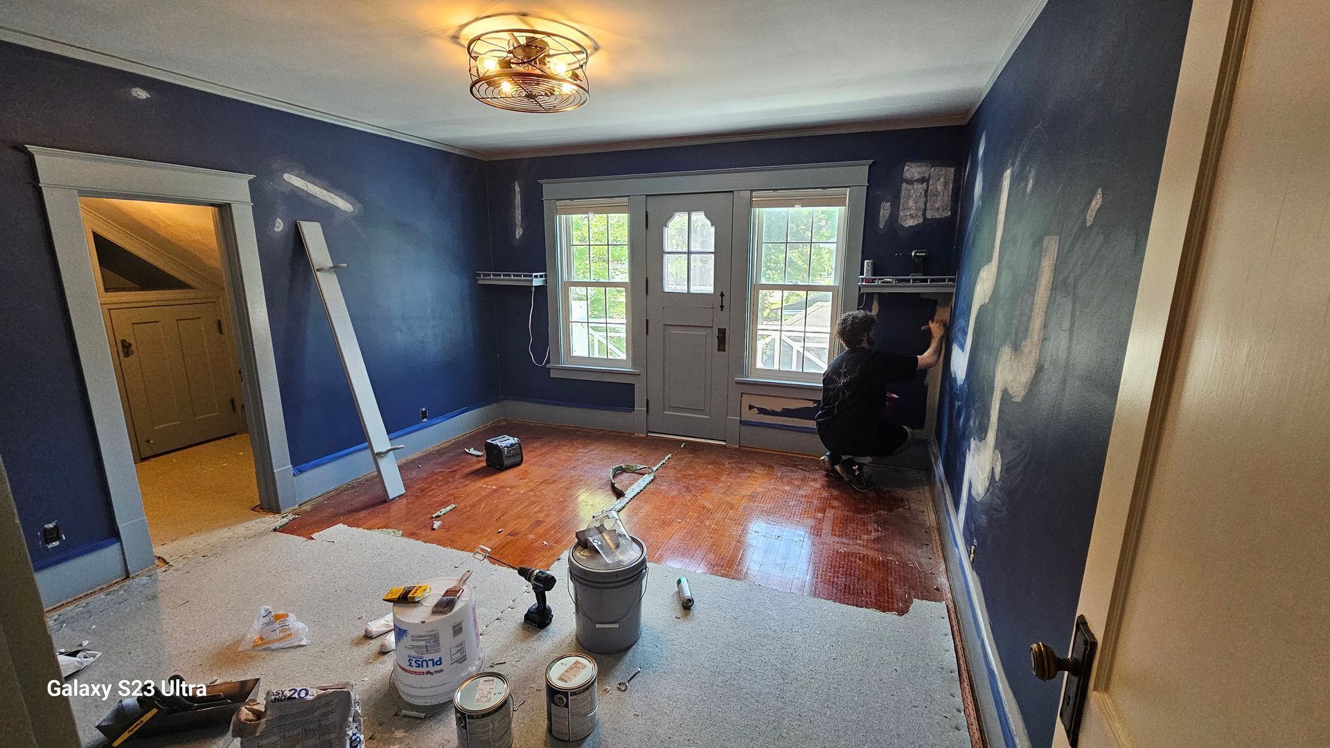 A room with blue walls and a wooden floor is being painted