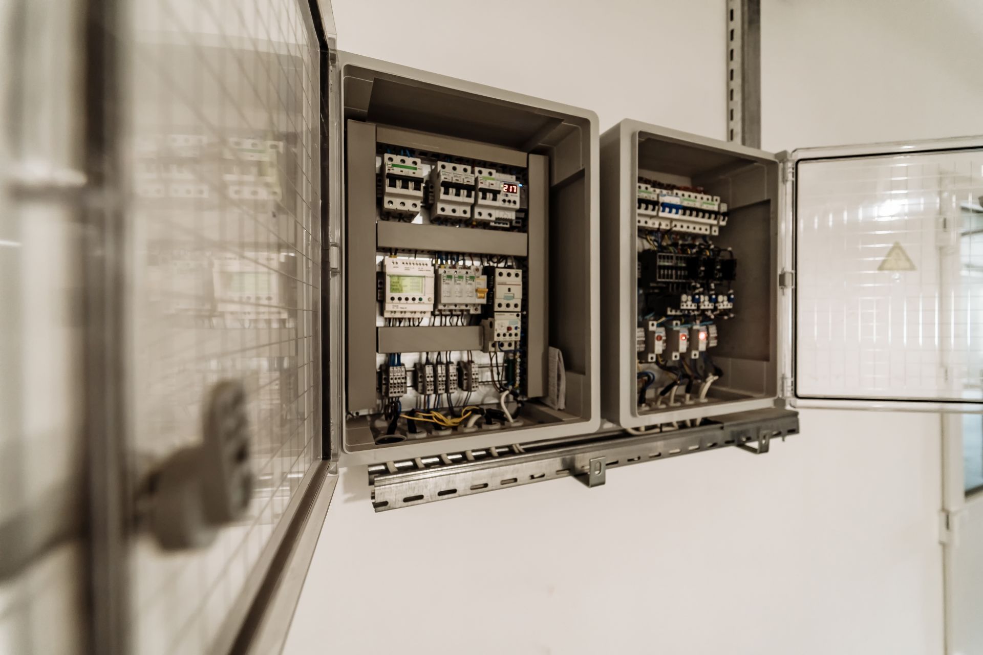 Open electrical control panels mounted on a white wall, filled with wiring and components.