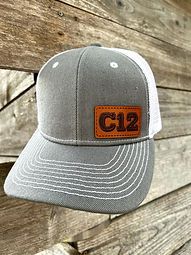 A baseball cap with a leather patch on it is hanging on a wooden wall.