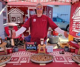 A man is standing behind a table with plates of food on it.