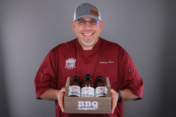 A man in a chef 's uniform is holding a box of bbq sauces.