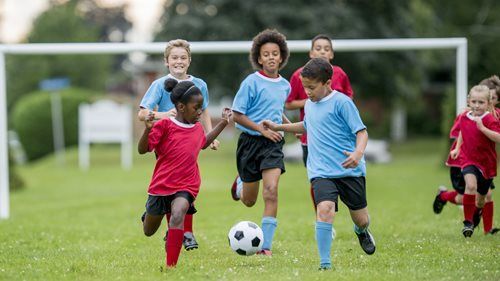Kids playing soccer on a grassy field; two teams, red and blue jerseys, running after the ball.