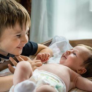 Smiling child looking at a baby lying on a changing table.