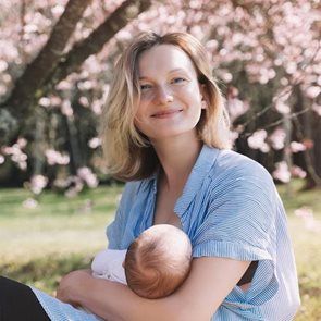 Woman in blue nursing a baby outdoors under pink blossoms.