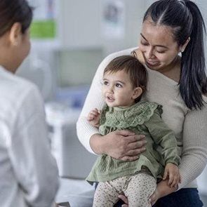Woman holding a baby at a doctor's appointment. The baby looks toward the doctor.