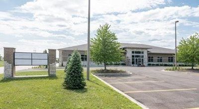 Building exterior with a sign, trees, and parking area under a cloudy sky.