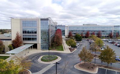 Modern office buildings with glass windows, fall foliage, and a circular drive.