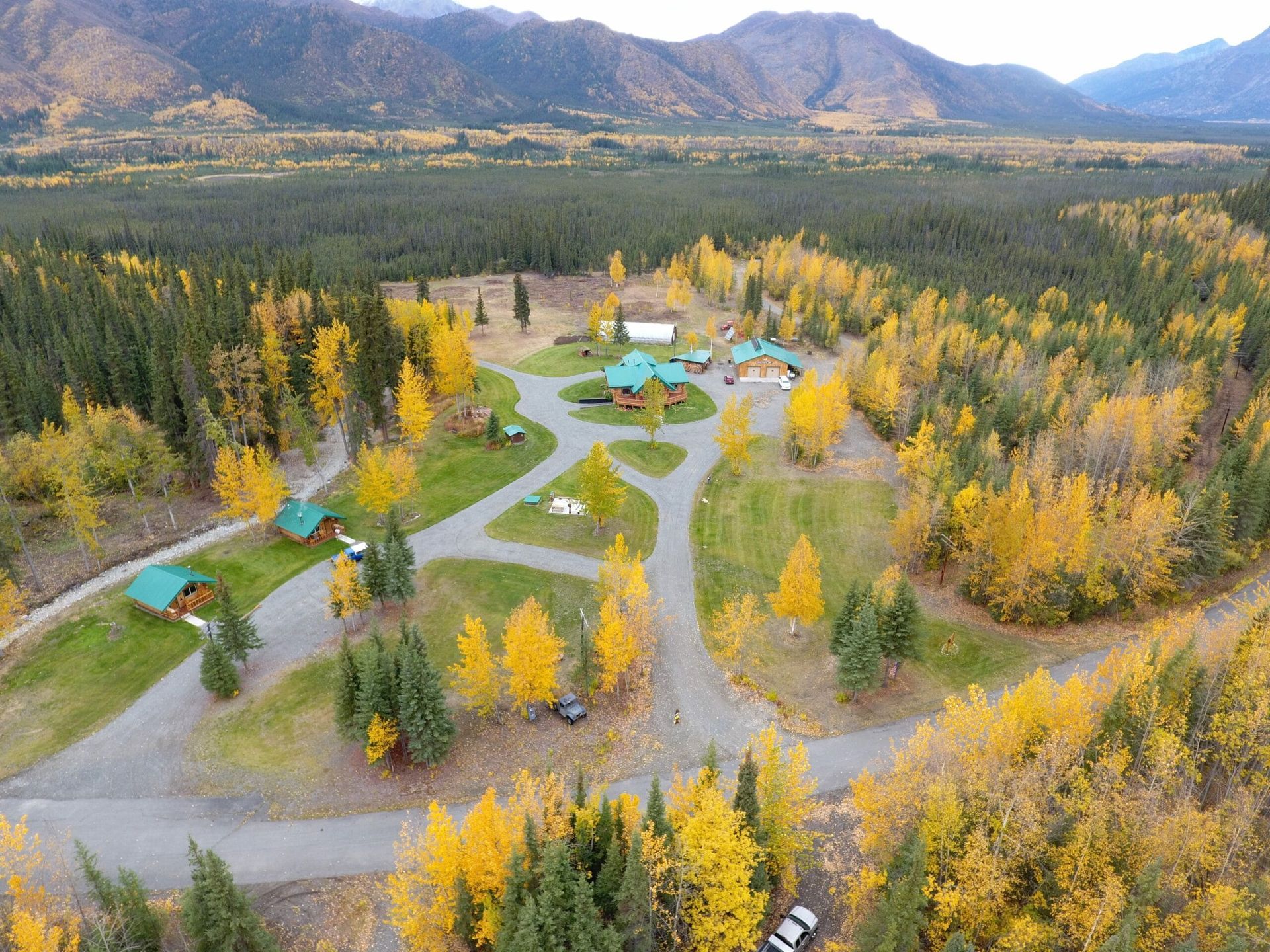 An aerial view of a house in the middle of a forest with mountains in the background.