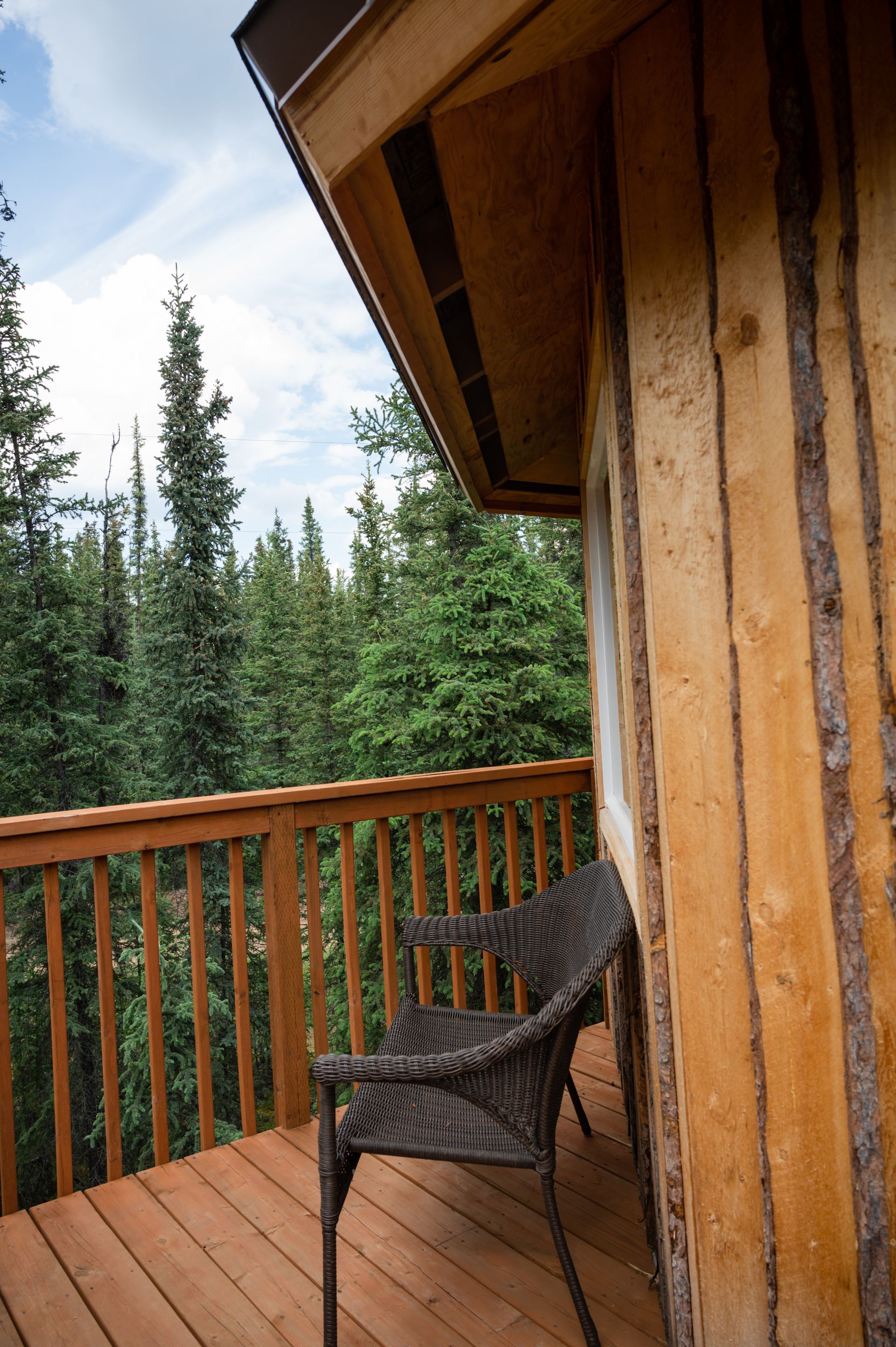 Wooden cabin balcony with a wicker chair overlooking a forest.