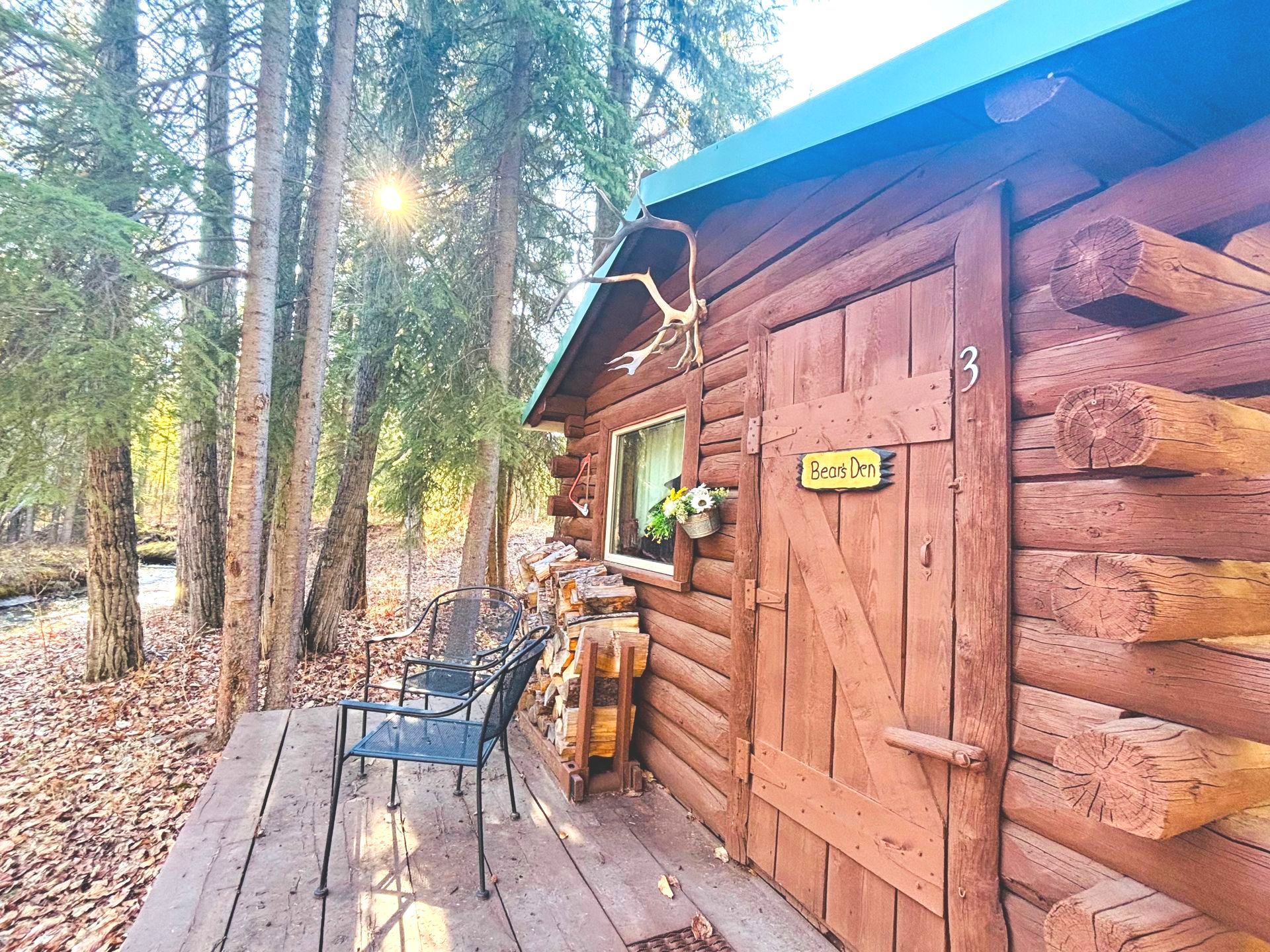 Log cabin with wooden exterior, window, door, and flowers on a grassy lawn.