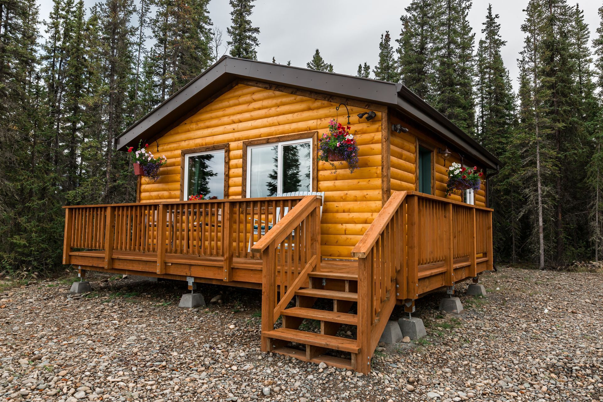 Small, wooden cabin with brown roof and deck, surrounded by trees.