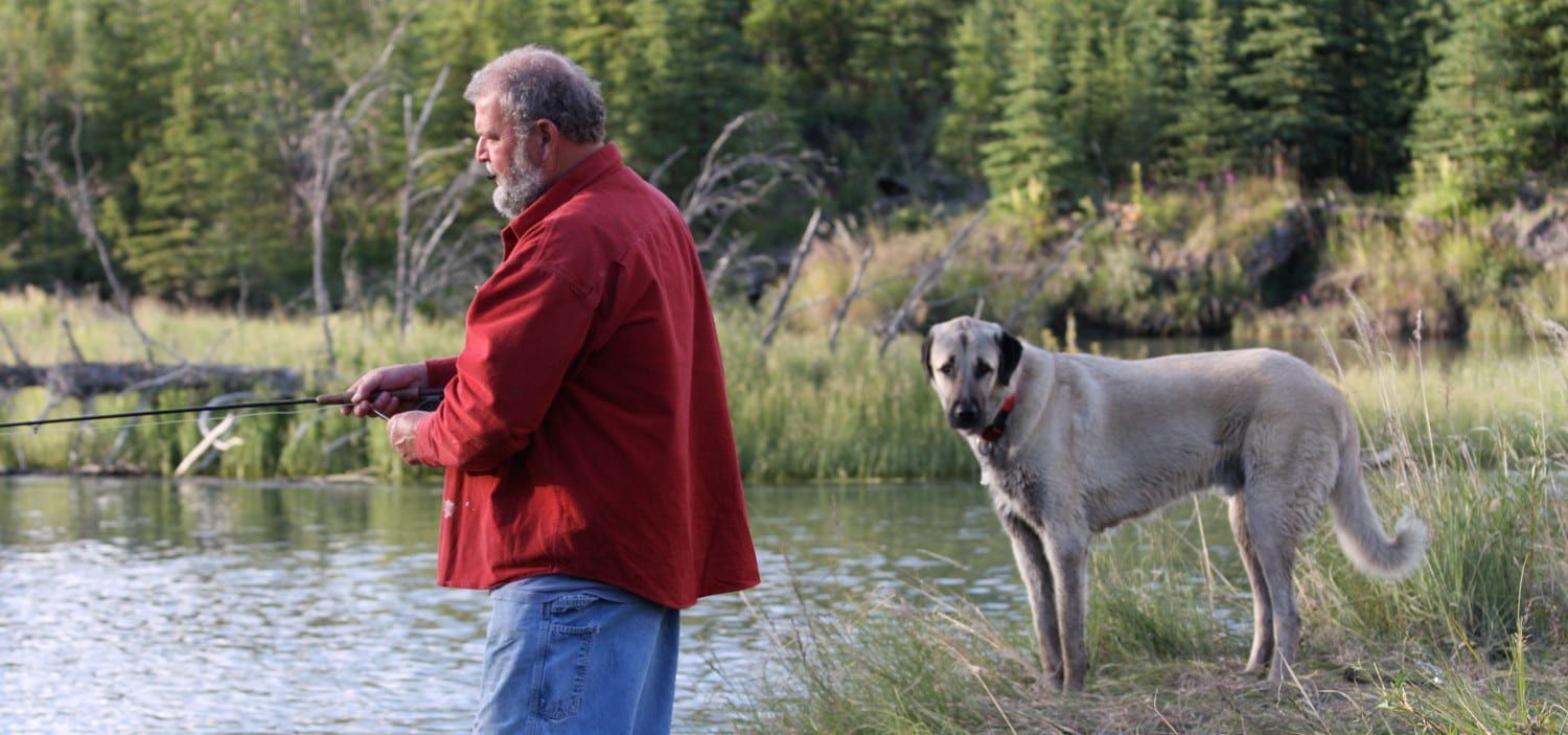 A man is fishing in a lake with his dog.