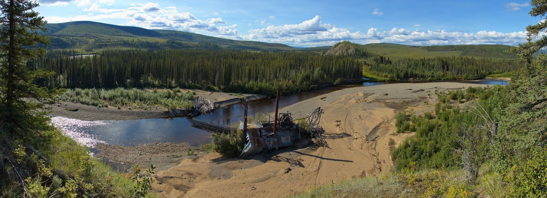 A wide river flows through a valley with forested hills under a blue sky.